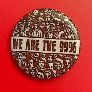 Könnte beinhalten: Ein brauner und weißer Knopf mit einem Schwarzweißbild einer Menschenmenge und dem Text "WE ARE THE 99%".