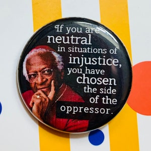 Könnte beinhalten: Ein schwarz-weißer Knopf mit einem Zitat von Desmond Tutu. Das Zitat lautet: "Wenn du in Situationen der Ungerechtigkeit neutral bist, hast du dich für die Seite des Unterdrückers entschieden."