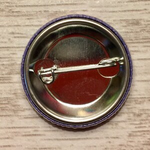 May include: The back of a purple button with a metal pin and a silver backing.