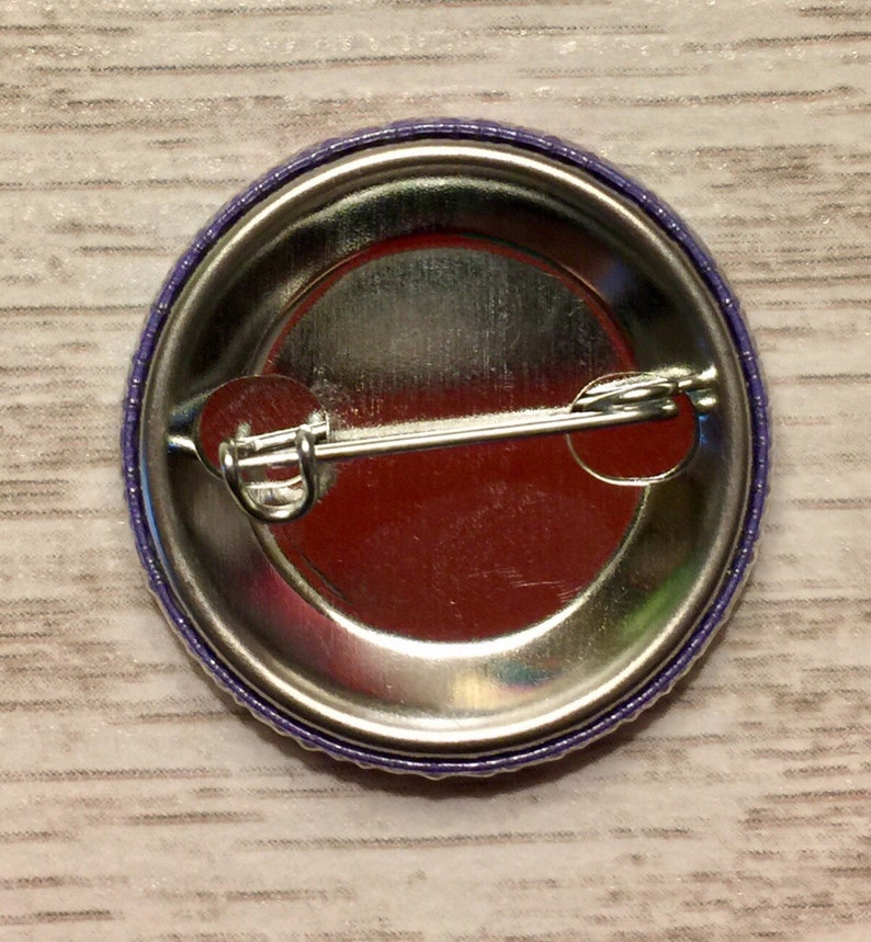 May include: The back of a purple button with a metal pin and a silver backing.