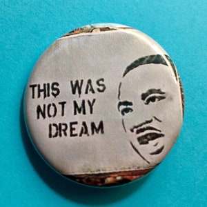 May include: A white button with a black and white image of Martin Luther King Jr. with the text "This was not my dream" printed on it.