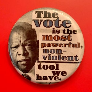 May include: A black and white button with a photo of John Lewis and the text "The vote is the most powerful, non-violent tool we have."