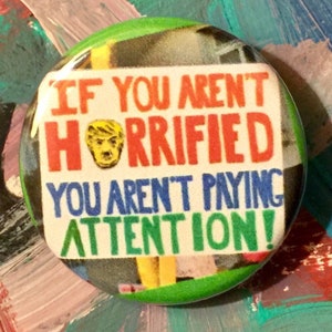 May include: A green, white, red, and blue button with a picture of a person and the text "IF YOU AREN'T HORRIFIED YOU AREN'T PAYING ATTENTION!"