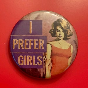 Könnte beinhalten: Ein lila und weißer Knopf mit dem Text "I prefer girls" und einem Vintage-Bild einer Frau in einem roten Kleid.