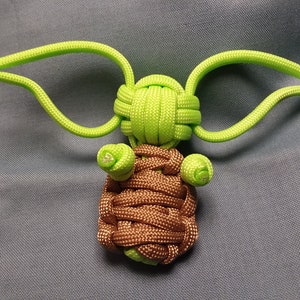 May include: A green and brown paracord knot, resembling a popular fictional character, with large ears and a small body.