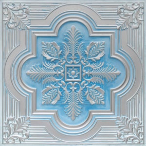 Op de afbeelding: Een decoratieve plafondtegel met een zilveren en blauw ontwerp. De tegel heeft een centraal bloemmotief met ingewikkelde details.