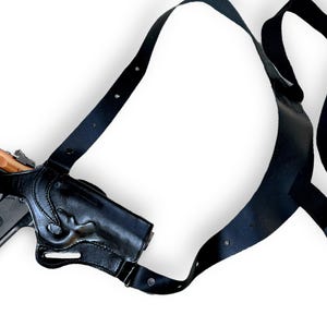May include: Black leather shoulder holster with a handgun. The holster has a molded design to fit the gun and adjustable straps. The handgun is silver and black with a brown grip. The holster is designed to be worn under the arm.