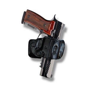 May include: A black and silver handgun with a brown wooden grip and the brand name "SIG SAUER" is shown in a black leather holster. The handgun is angled slightly to the left against a white background.
