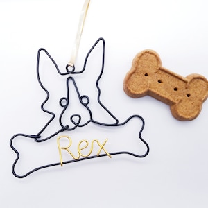 May include: Black wire dog ornament with a bone shape and the name "Rex" written in gold wire. A brown dog biscuit is also in the image.