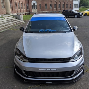 May include: A silver Volkswagen Golf with a blue windshield banner that reads "Fuel To Inspire" and a black front bumper with a "UNITRONIC" logo.