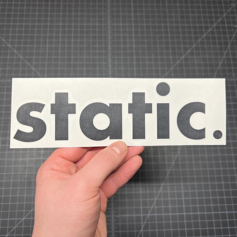 May include: A rectangular white sticker featuring the word static. printed in a bold, dark grey sans-serif font. The text includes a full stop at the end, and the letters have a subtle, fine-textured pattern visible across their surface.