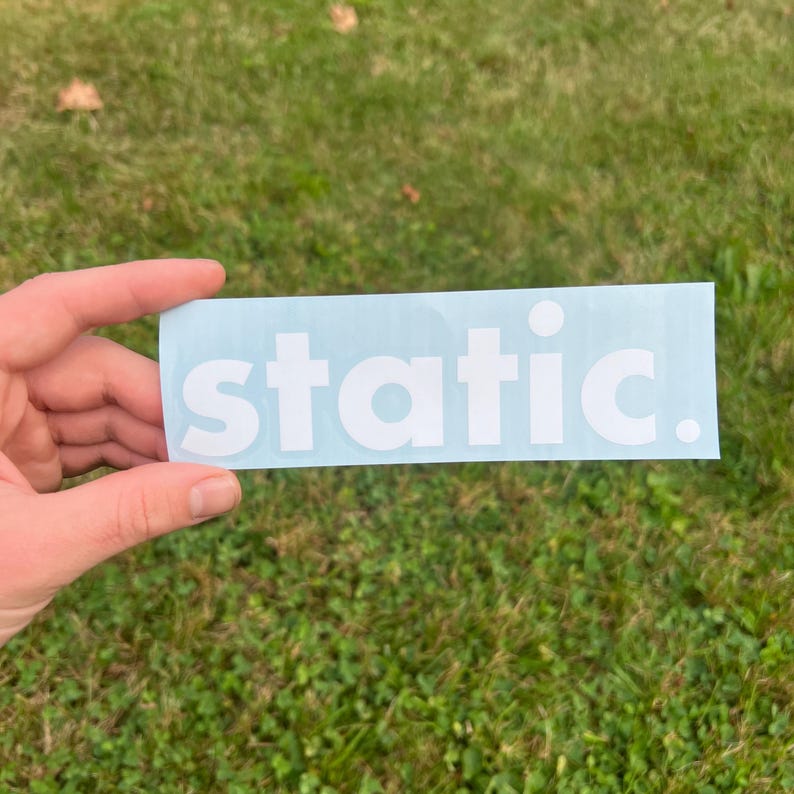 May include: A rectangular light blue vinyl decal featuring the word static in bold white lowercase letters followed by a full stop. The sticker has a smooth finish and is presented on a clear backing sheet, displaying clean typography and a simple design.
