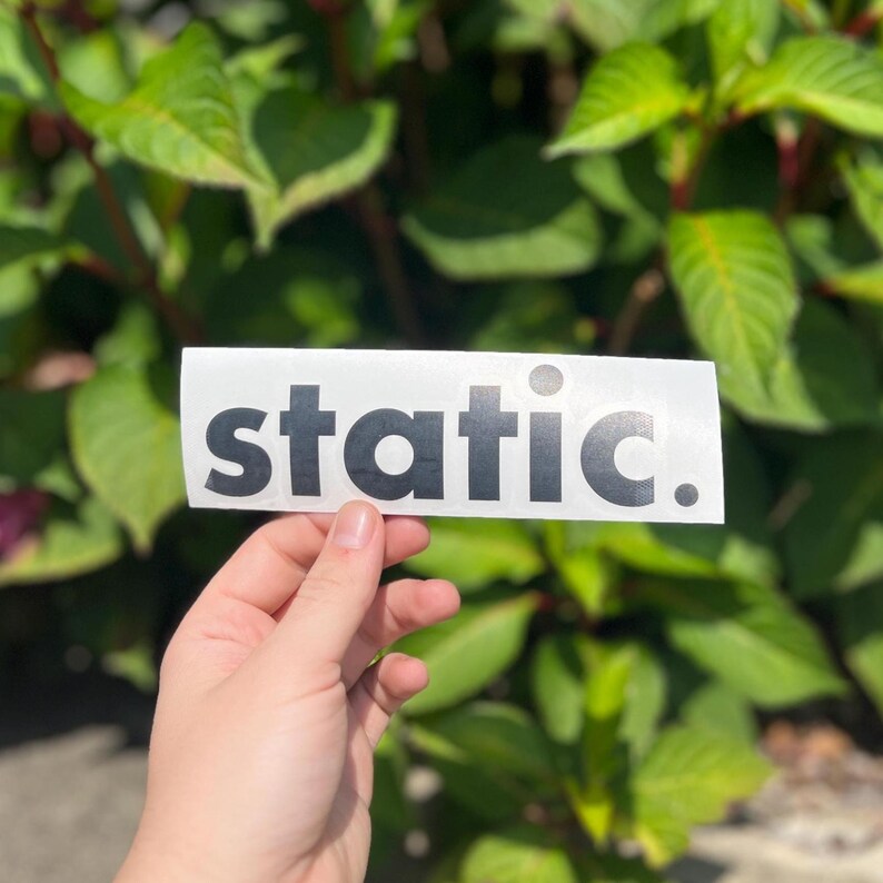 May include: A rectangular white sticker featuring the word static. printed in a bold, black, sans-serif font. The sticker has a clean, minimalist design with a full stop at the end of the text, presented on a clear backing material.