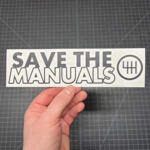 May include: A white sticker with black text that reads "SAVE THE MANUALS" with a black and white gear shift pattern icon.