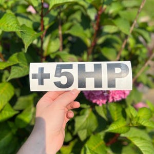 May include: A rectangular white vinyl decal featuring the bold black text +5HP in a clean sans-serif font. The sticker has a smooth, matte finish and is presented on a clear backing, designed for application on smooth surfaces like vehicle windows.