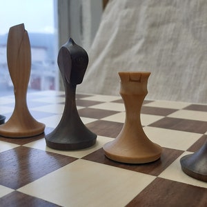 Pode incluir: Um conjunto de pe&ccedil;as de xadrez de madeira num tabuleiro de xadrez. As pe&ccedil;as s&atilde;o feitas de madeira escura e clara e est&atilde;o dispostas em fila. As pe&ccedil;as incluem um pe&atilde;o, um bispo, um cavalo e uma torre.