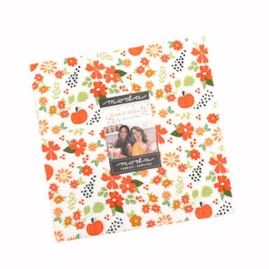 May include: A square stack of fabric squares featuring a white background with an orange and green floral pattern interspersed with small orange pumpkins and black dotted accents. A central label reads moda, Birch & Willow, and moda fabrics.