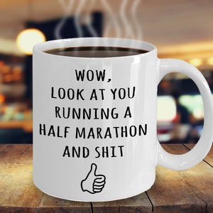 May include: White ceramic coffee mug with black text that reads "WOW, LOOK AT YOU RUNNING A HALF MARATHON AND SHIT" with a thumbs up icon.