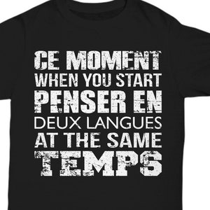 May include: Black t-shirt with white text that reads "CE MOMENT WHEN YOU START PENSER EN DEUX LANGUES AT THE SAME TEMPS".