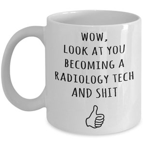 May include: White ceramic coffee mug with black text that reads "WOW, LOOK AT YOU BECOMING A RADIOLOGY TECH AND SHIT" with a thumbs up icon.