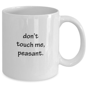 May include: White ceramic mug with a curved handle. The mug features the phrase "don't touch me, peasant" in black, sans-serif font. The mug is designed for hot beverages and has a standard size.