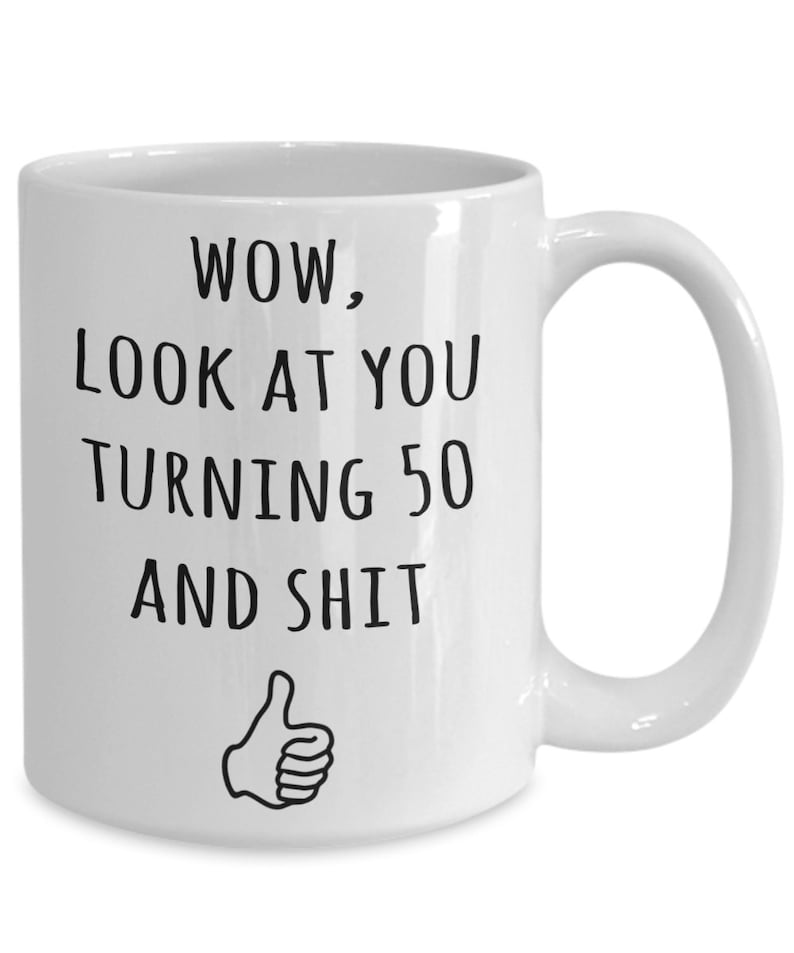 May include: White ceramic coffee mug with black text that reads "WOW, LOOK AT YOU TURNING 50 AND SHIT" with a thumbs up icon.