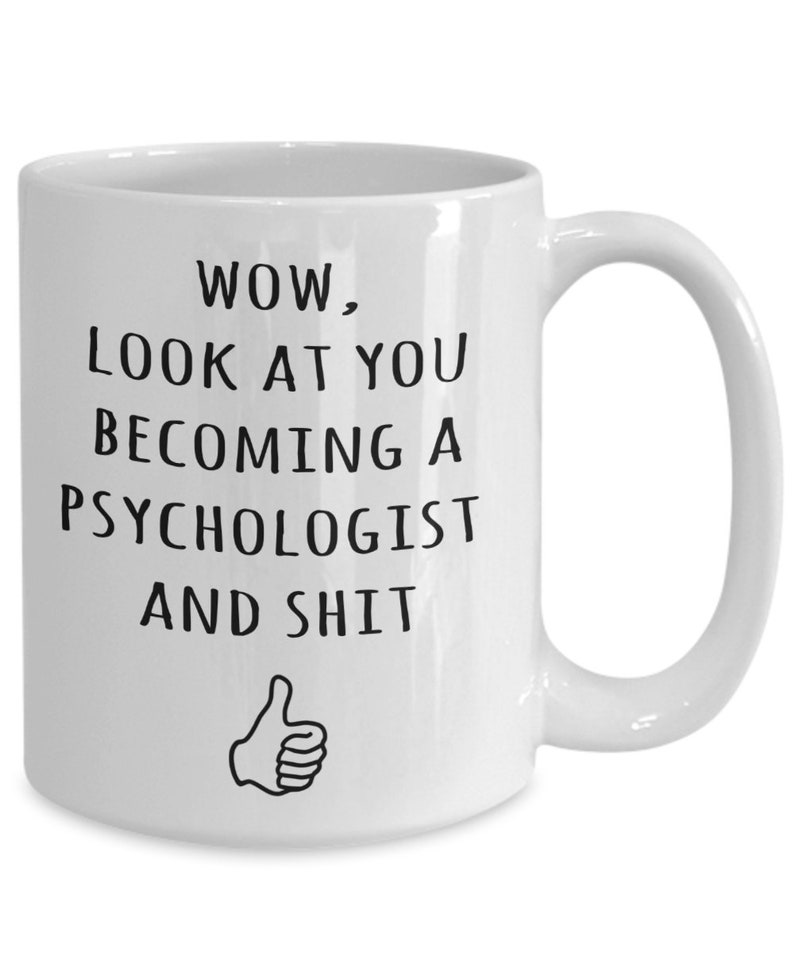May include: White ceramic mug with a black text that reads "WOW, LOOK AT YOU BECOMING A PSYCHOLOGIST AND SHIT" with a thumbs-up graphic. The mug has a curved handle and is designed for hot beverages.