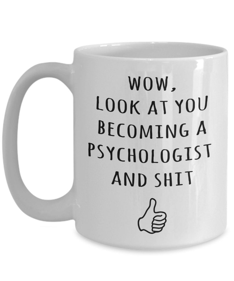 May include: White ceramic mug with a black text that reads "WOW, LOOK AT YOU BECOMING A PSYCHOLOGIST AND SHIT" with a thumbs-up graphic. The mug has a curved handle.