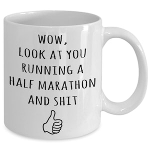 May include: White ceramic coffee mug with black text that reads "WOW, LOOK AT YOU RUNNING A HALF MARATHON AND SHIT" with a thumbs up icon below the text.