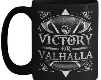 Puede incluir: Taza de cerámica negra con un diseño gráfico blanco. El diseño presenta las palabras "VICTORY OR VALHALLA" en una fuente desgastada, junto con imágenes de hachas y escudos vikingos. La taza tiene un asa curvada.