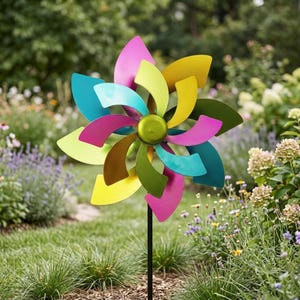 Puede incluir: Un colorido molinillo de jardín con diseño de flor. El molinillo presenta aspas curvas en tonos rosa, amarillo, azul, verde y marrón, con un centro verde. Está montado sobre un poste de metal negro en un jardín.