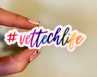 Op de afbeelding: Een witte sticker met de tekst "#vettechlife" in regenboogkleuren. De sticker wordt vastgehouden door een vinger met kleurrijke nagellak.