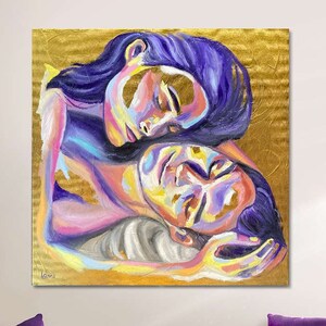 May include: A large square canvas art piece featuring a colorful painting of two figures embracing. The figures are painted in shades of purple, pink, yellow, and blue against a gold background. The artwork hangs above a purple sofa with decorative pillows.