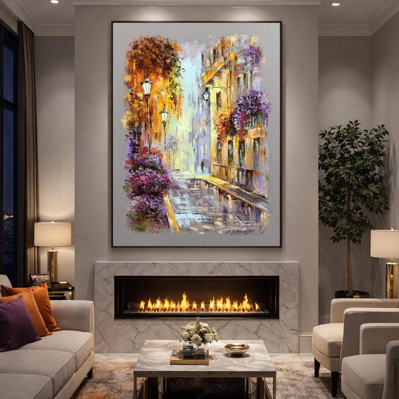 May include: An oil painting depicts a European street scene with buildings, streetlights, and a cobblestone street. The artwork features a palette of warm colors, including orange, yellow, and purple, creating a vibrant and inviting atmosphere. The painting is framed and mounted above a fireplace.