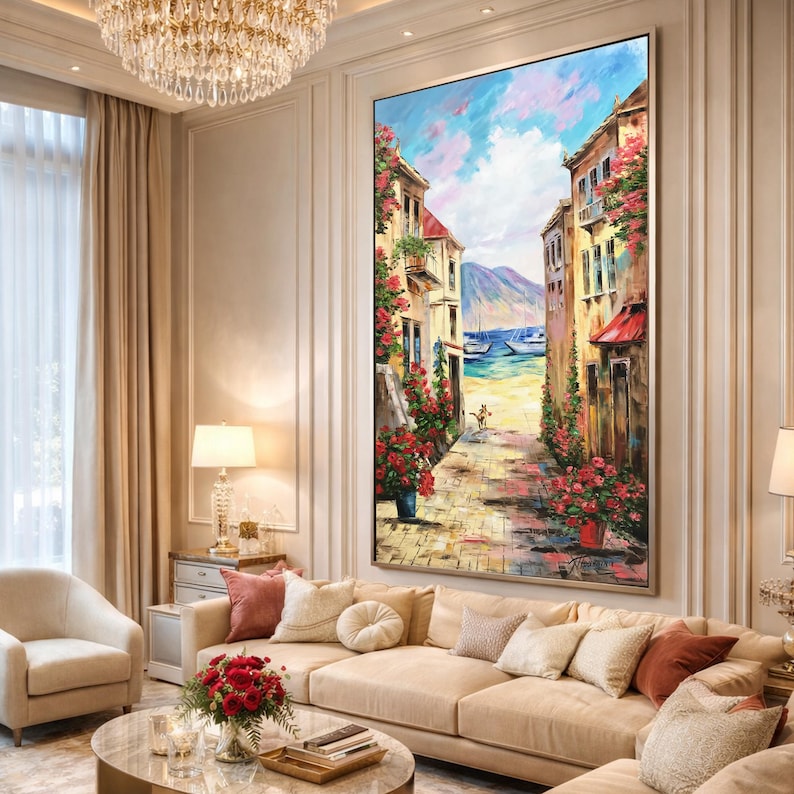 May include: Large framed oil painting depicting a European street scene. The artwork features buildings with red-tiled roofs, vibrant red flowers, and a pathway leading to the sea. The sky is a mix of blue and white, with mountains in the distance.