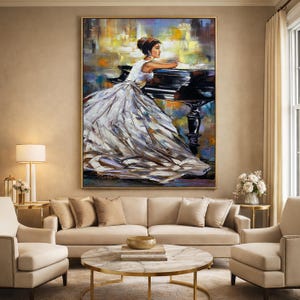 May include: An oil painting depicts a woman in a white gown leaning on a black piano. The artwork has a gold frame and is displayed above a beige sofa. The background features abstract brushstrokes in yellow, blue, and orange.