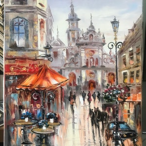 May include: A painting of a European city street scene with a horse-drawn carriage, a cafe with orange umbrellas, and a church in the background. The painting is done in a realistic style with a focus on detail.