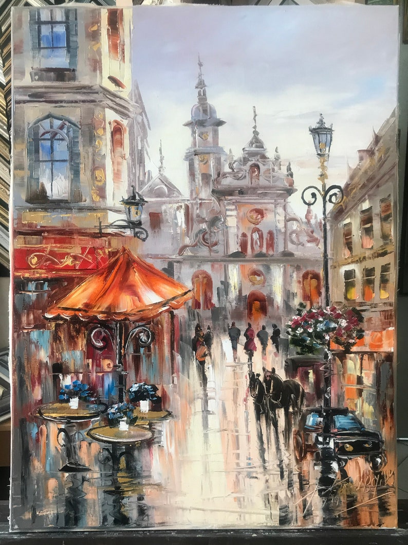 May include: A painting of a European city street scene with a horse-drawn carriage, a cafe with orange umbrellas, and a church in the background. The painting is done in a realistic style with a focus on detail.