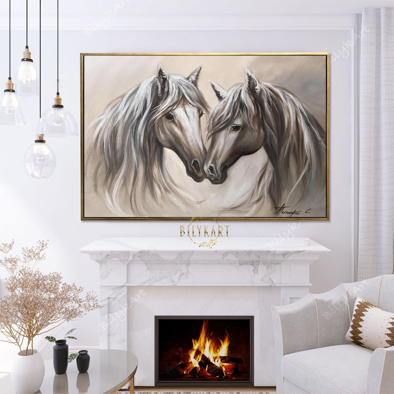 May include: An oil painting of two white horses with flowing manes, their heads touching. The artwork is framed in gold and hangs above a fireplace. The painting has a soft, neutral color palette with a signature in the bottom right corner.