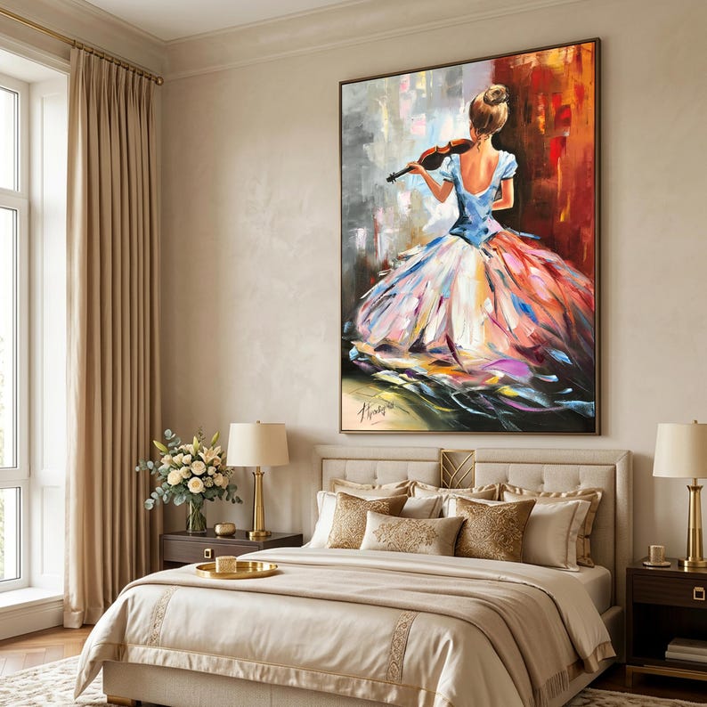 May include: An oil painting shows a woman playing a violin, seen from behind, in a blue top and a vibrant, flowing dress. The artwork is framed and hangs above a bed with beige bedding and gold accents. The room has neutral tones.