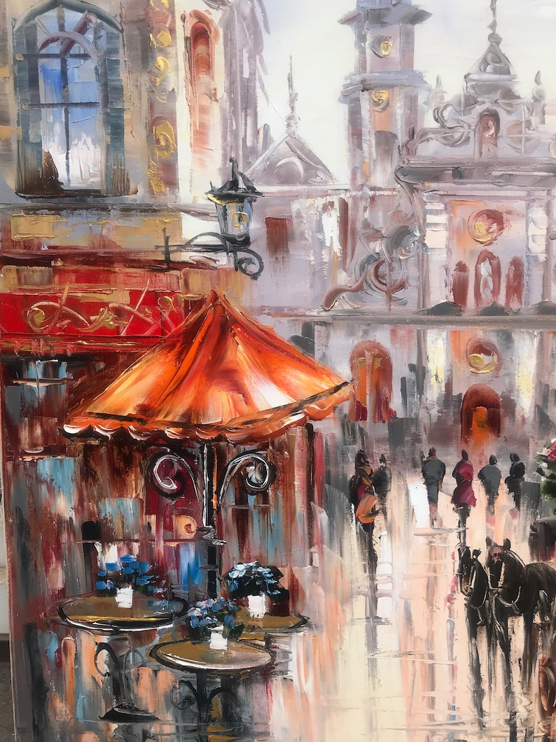 May include: A painting of a street scene with an orange umbrella over a cafe table. The cafe is located in a European city with tall buildings and a cobblestone street. The painting is done in a painterly style with loose brushstrokes and vibrant colors.