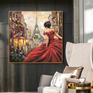 Op de afbeelding: Olieverfschilderij van een vrouw in een rode jurk in Parijs, met de Eiffeltoren op de achtergrond. Het kunstwerk is ingelijst in een goudkleurige lijst. Het schilderij heeft een romantisch thema, met de nadruk op de vrouw en het Parijse stadsbeeld.