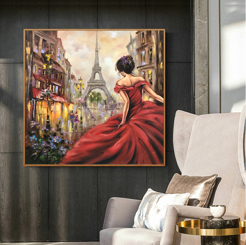 Op de afbeelding: Olieverfschilderij van een vrouw in een rode jurk in Parijs, met de Eiffeltoren op de achtergrond. Het kunstwerk is ingelijst in een goudkleurige lijst. Het schilderij heeft een romantisch thema, met de nadruk op de vrouw en het Parijse stadsbeeld.