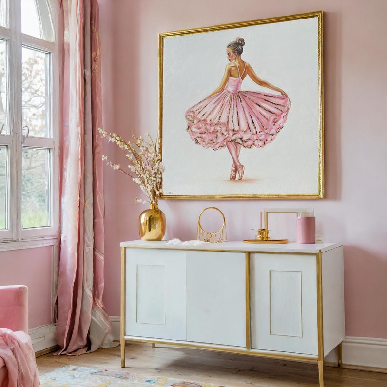 May include: A pink and gold ballerina painting in a gold frame hanging on a pink wall above a white cabinet with gold accents.