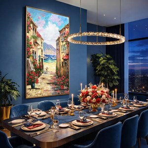 May include: A dining room with a large painting of a European street scene. The table is set for a formal dinner with blue velvet chairs, a floral centerpiece, and a modern chandelier. The painting features a cobblestone street, buildings, and boats.
