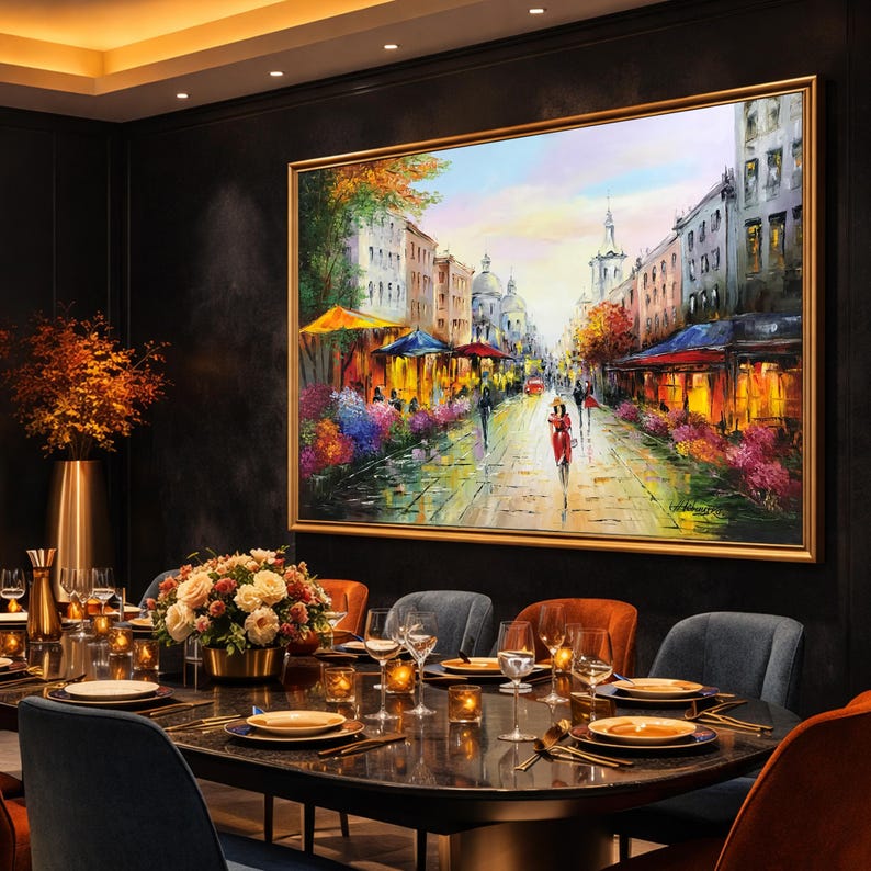 May include: A large framed oil painting depicts a European street scene with cafes, people, and colorful buildings. The artwork hangs above a dining table set for a meal, with flowers and candles.