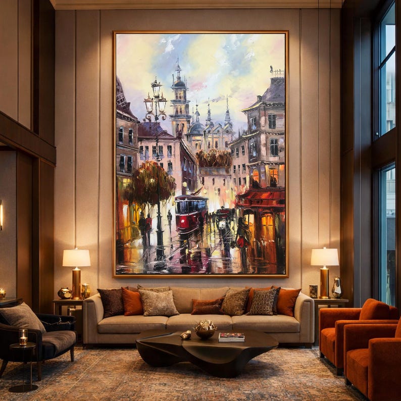 May include: Large framed oil painting of a European city street scene with a red tram, buildings, and figures. The artwork features a warm colour palette with highlights of red, yellow, and blue, creating a vibrant and detailed cityscape.