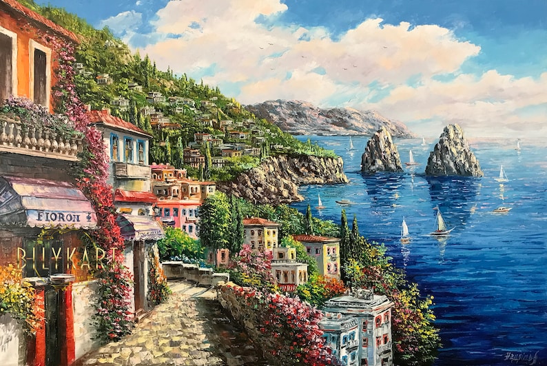 May include: A painting of a colorful Italian village nestled on a hillside overlooking a blue sea with two rocky islands in the distance. Sailboats dot the water and the sky is a bright blue with white clouds.