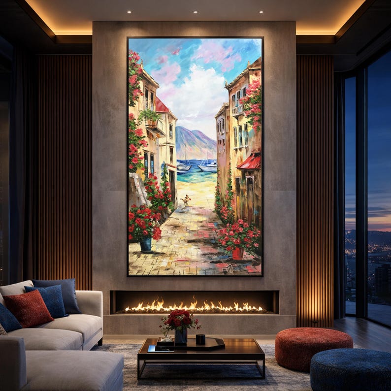 May include: Large framed oil painting depicting a coastal street scene. Buildings with red awnings and blooming red flowers line a cobblestone path leading to the sea. The sky is a mix of blue and pink hues, with boats visible in the distance.