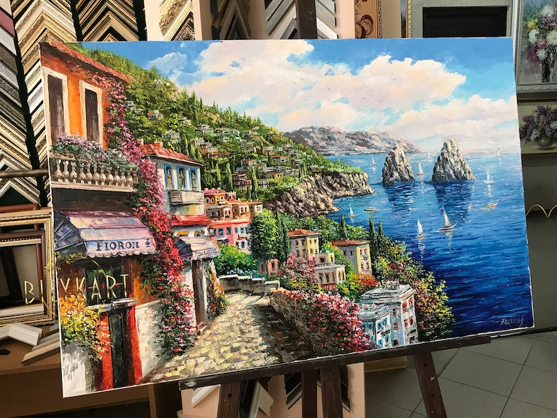 May include: A colorful oil painting depicting a coastal town with buildings, trees, and a blue ocean with sailboats. The painting has a bright, sunny sky with white clouds. The text "FIORONI" is visible on a building in the foreground.